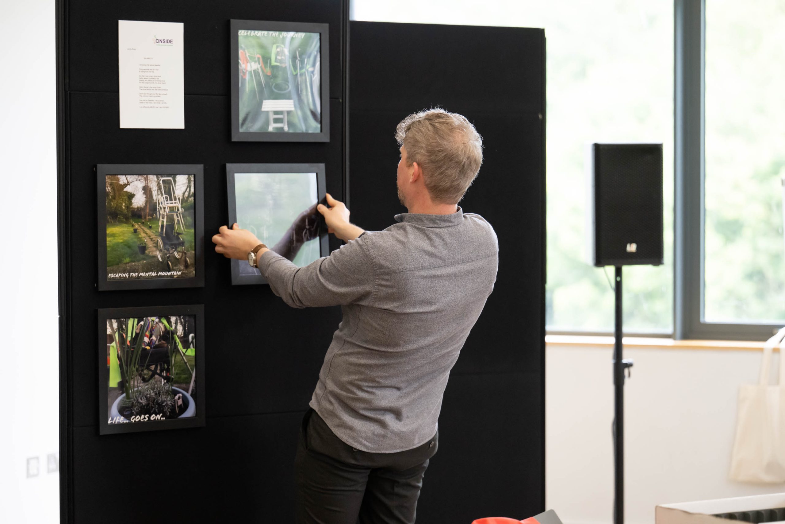 The photograph shows a man aligning a photograph to add to a display of photographs that are displayed on a board.  