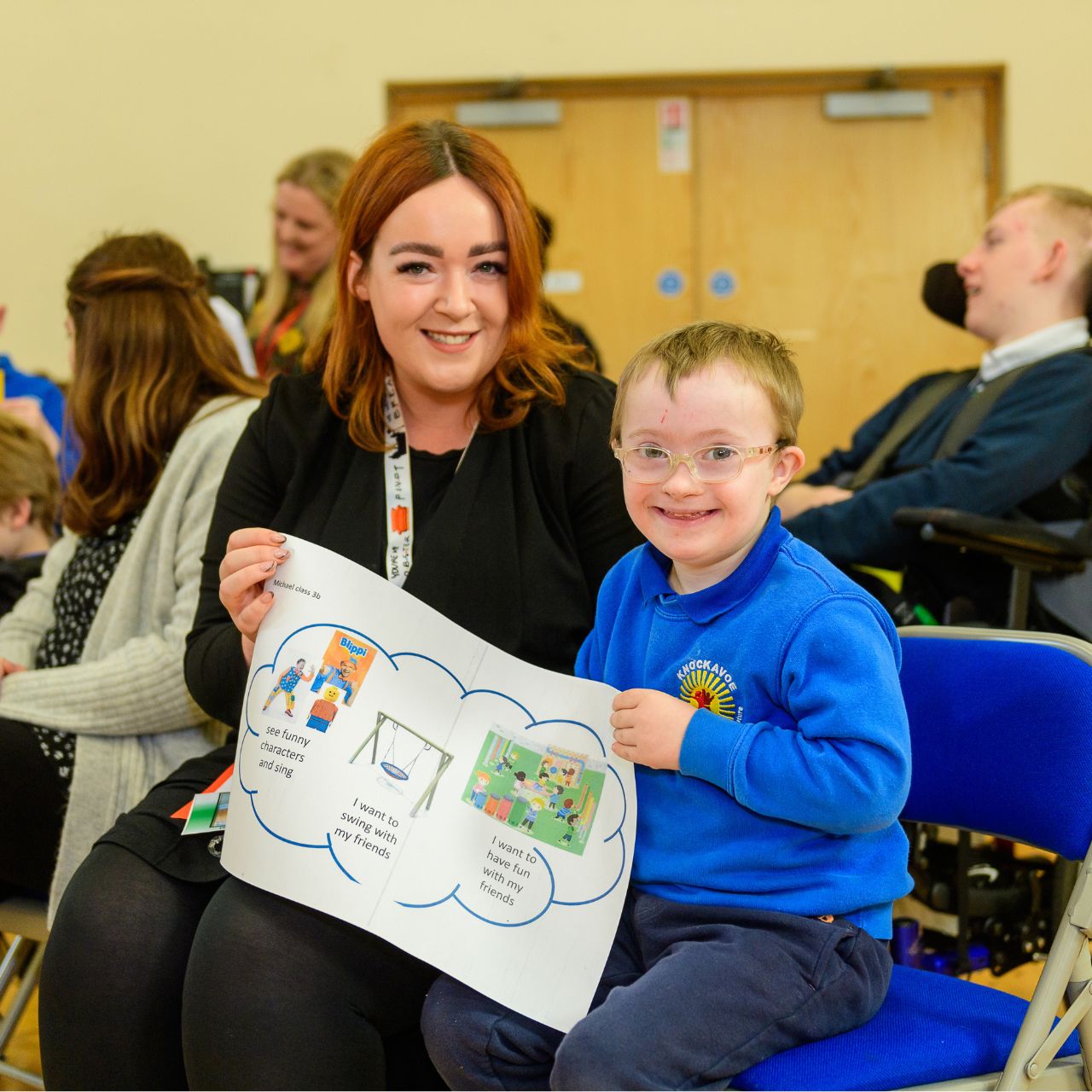 This photograph shows a young pupil and his teacher holding up a picture that he has drawn to show what he would like to see in an inclusive play park.   